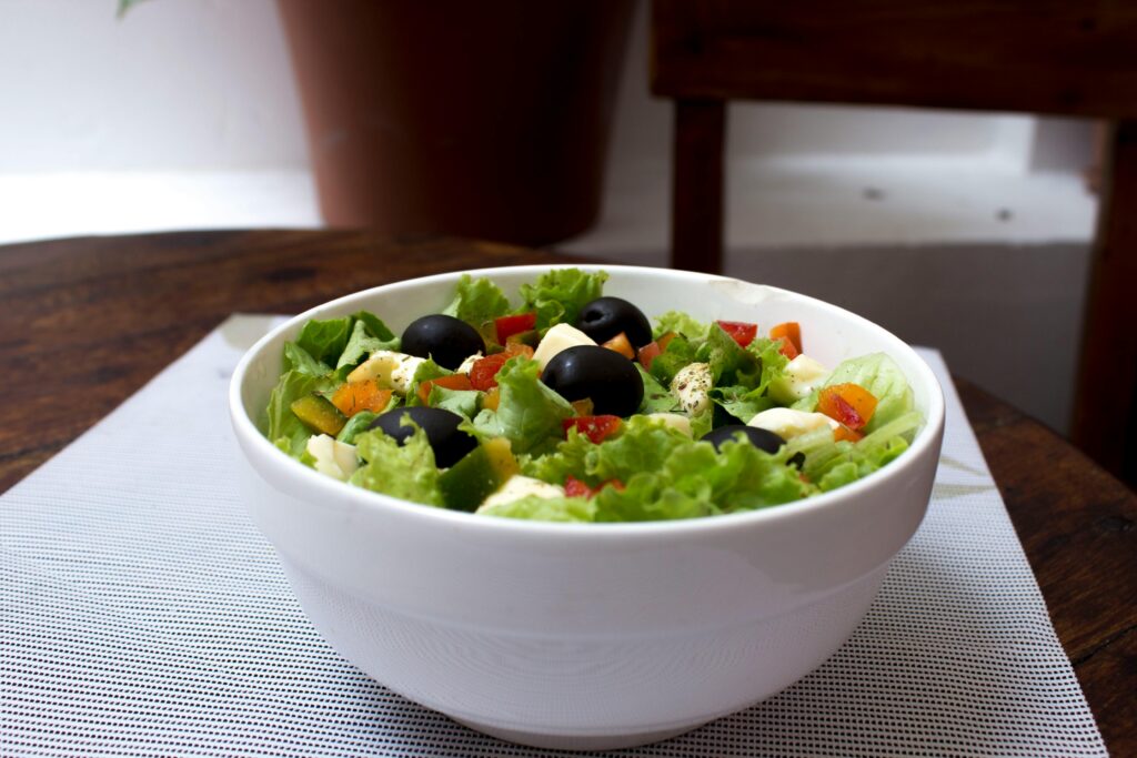 Delicious fresh salad with black olives, lettuce, and veggies in a white bowl indoors.